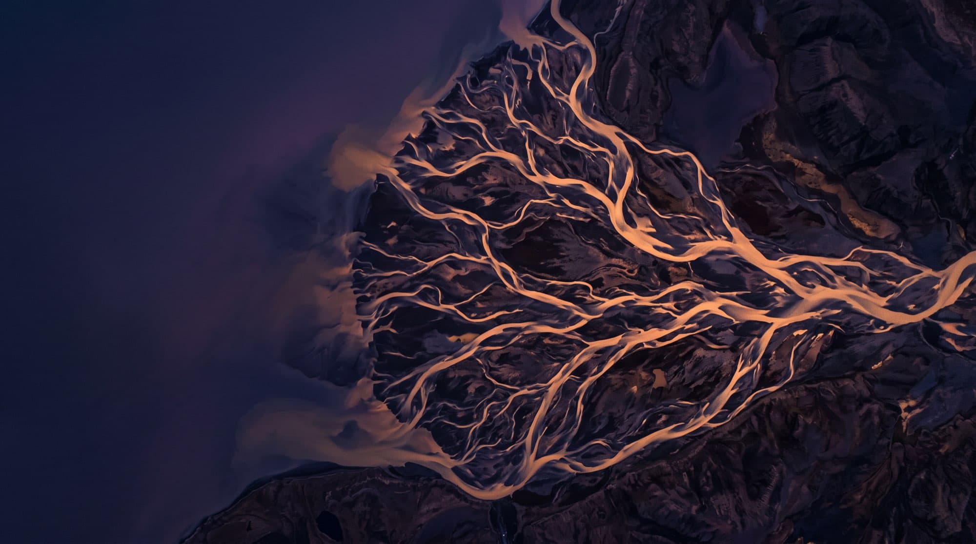 A river delta from the air at dusk: dozens of lit channels braiding across dark ground