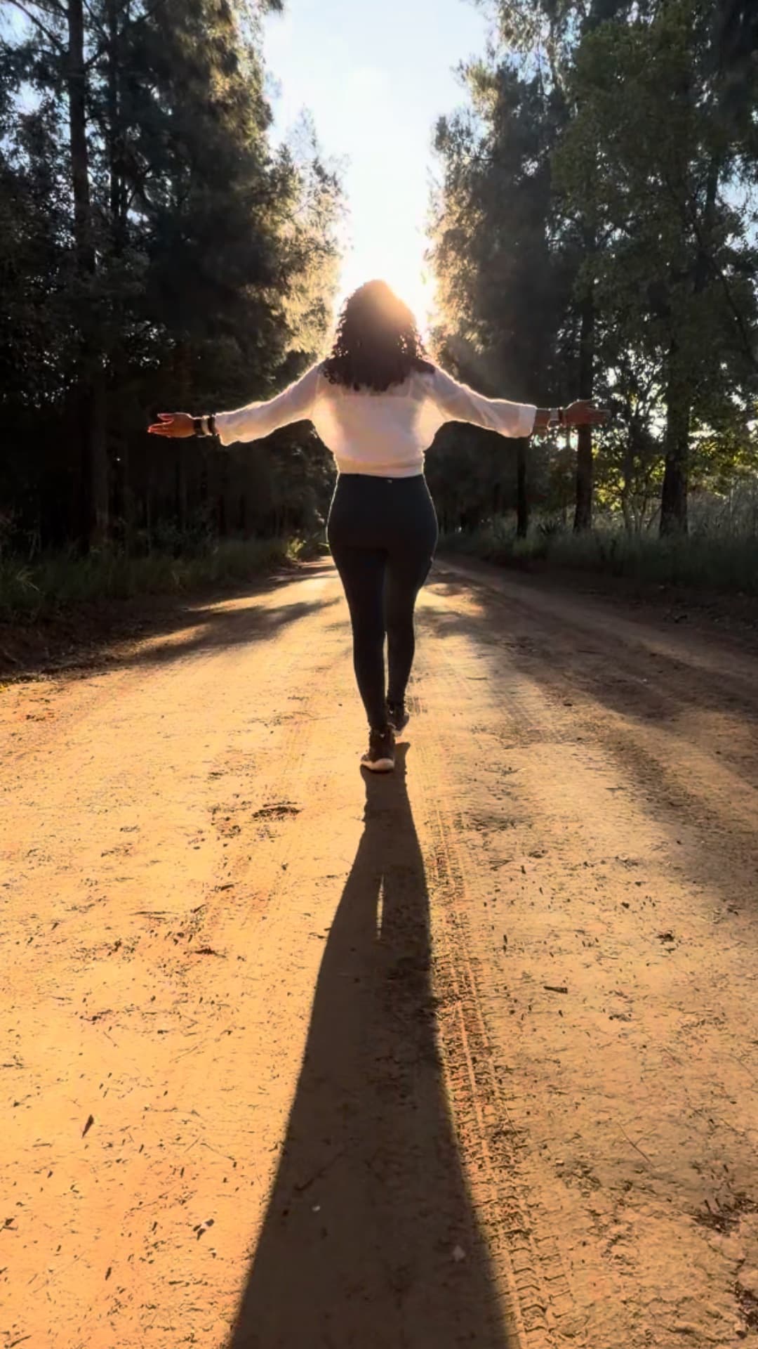 Latisha walking a sunlit road, arms open